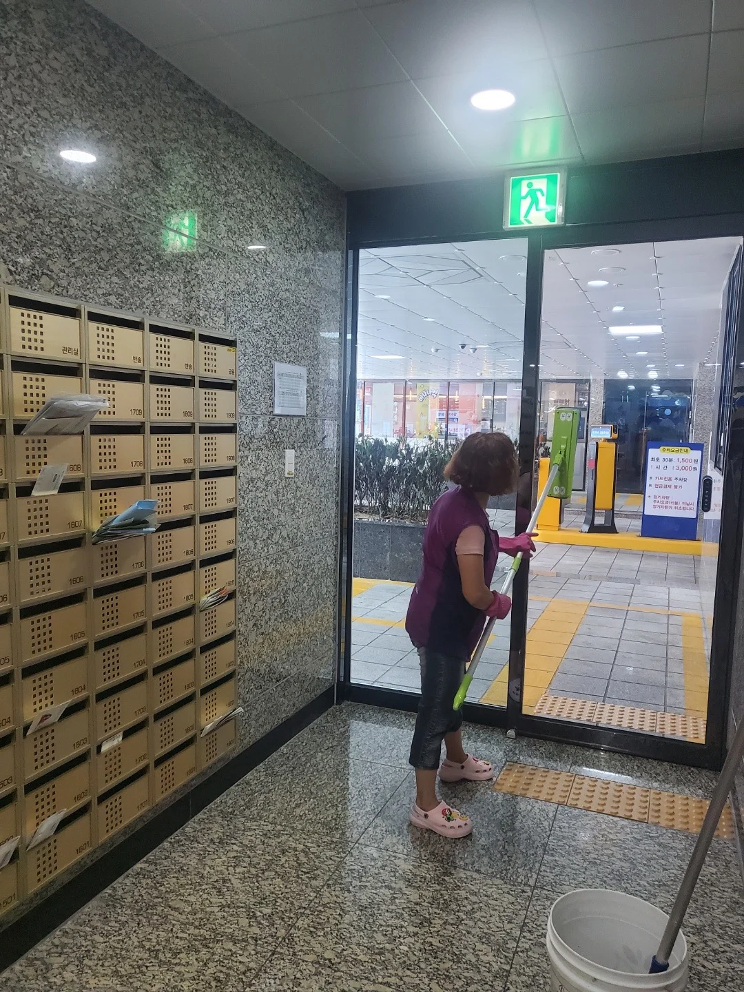 우편함 옆 출입구 유리문을 닦는 작업자