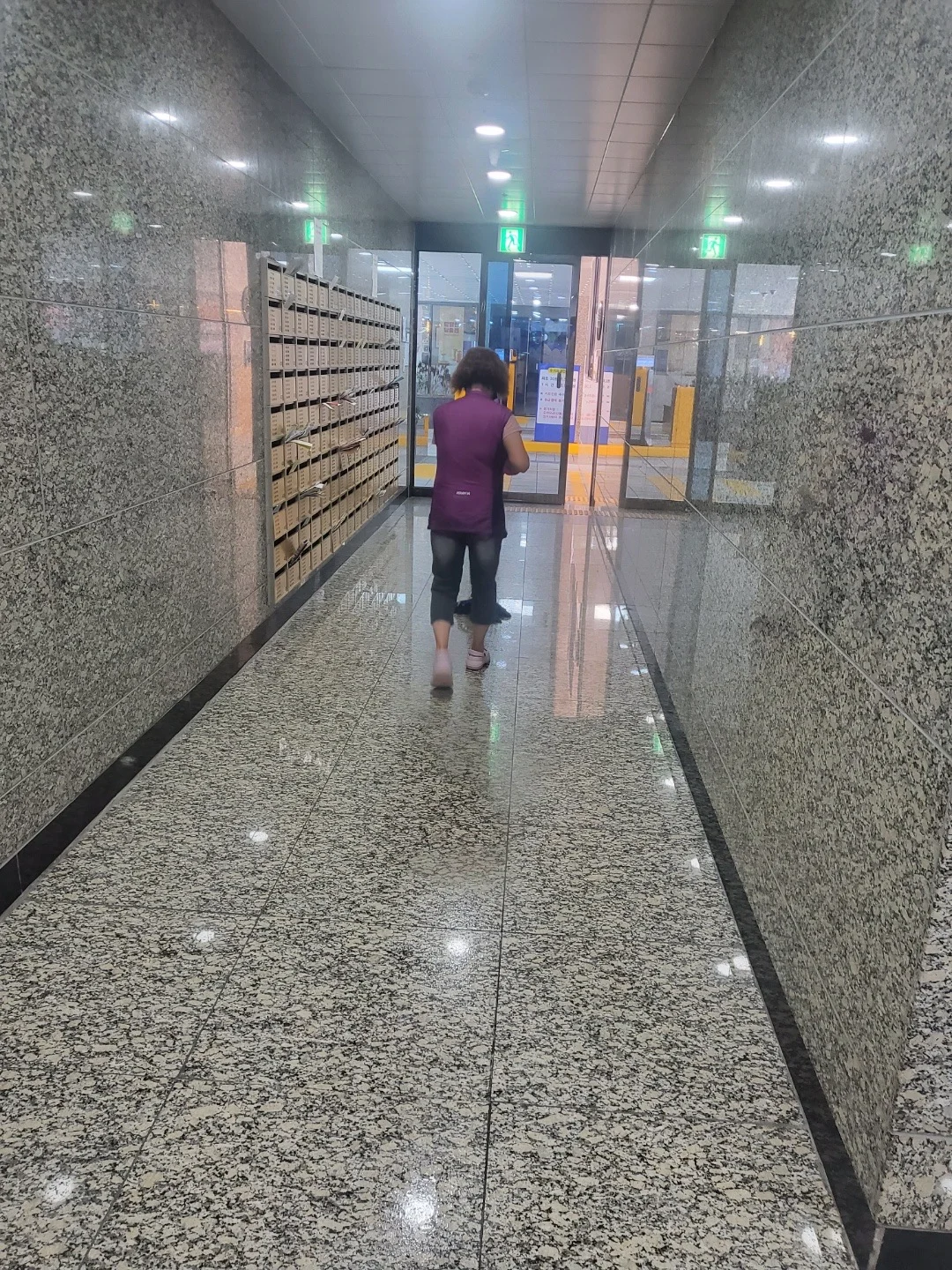 석재 마감 공용 복도에서 대걸레로 바닥을 닦는 작업자의 뒷모습