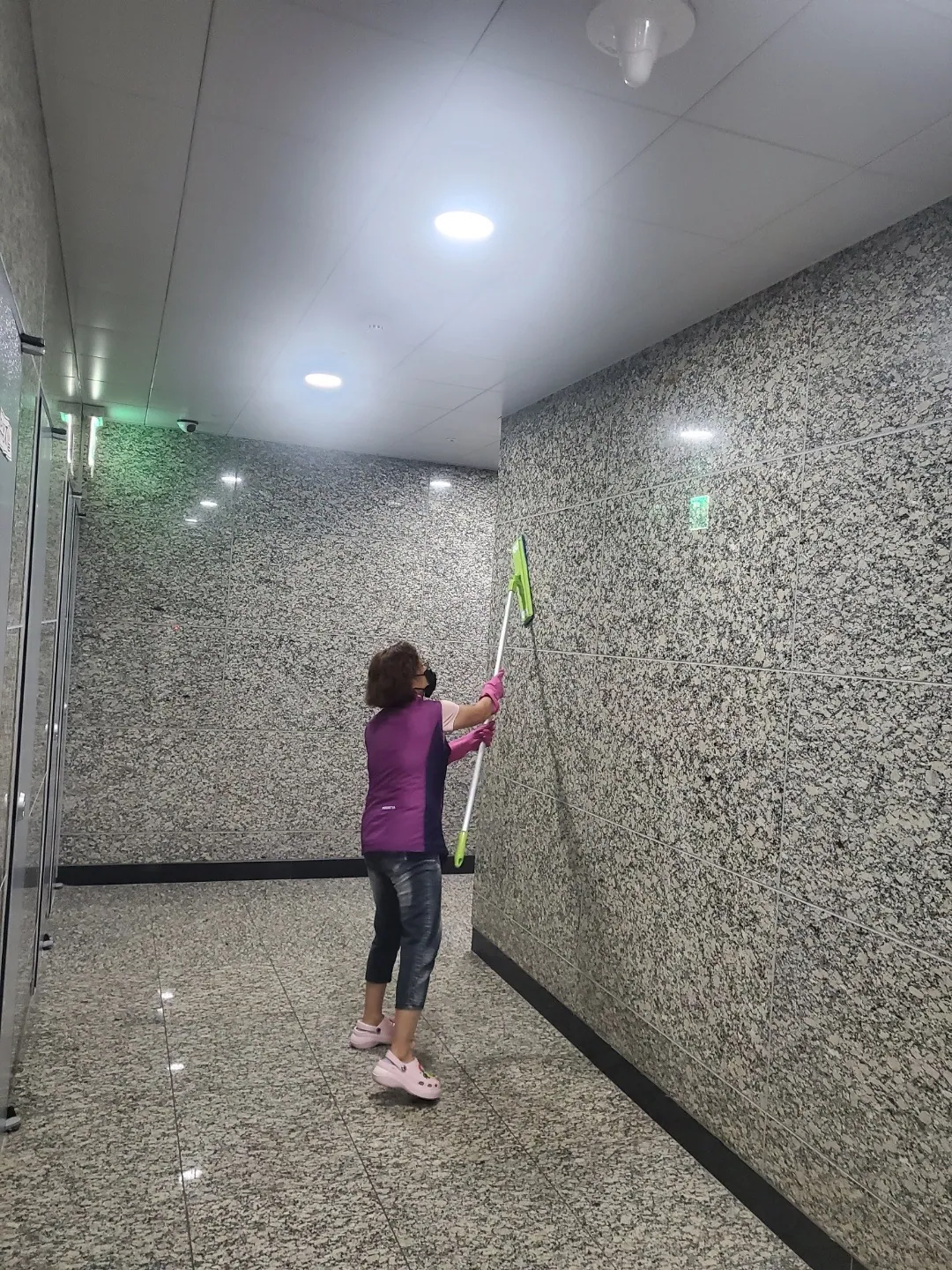 긴 밀대로 공용부 석재 벽면 위쪽을 닦는 작업자