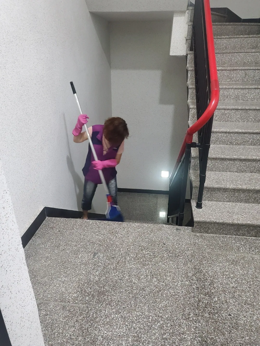 계단참에서 대걸레로 바닥을 닦는 작업자